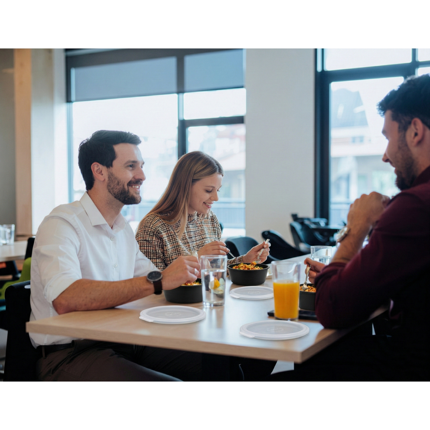 Glückliches Team bei der Firmenverpflegung von FooBi in der Mittagspause; gemeinsames Essen im Büro mit FooBi-Mehrwegverpackungen.
