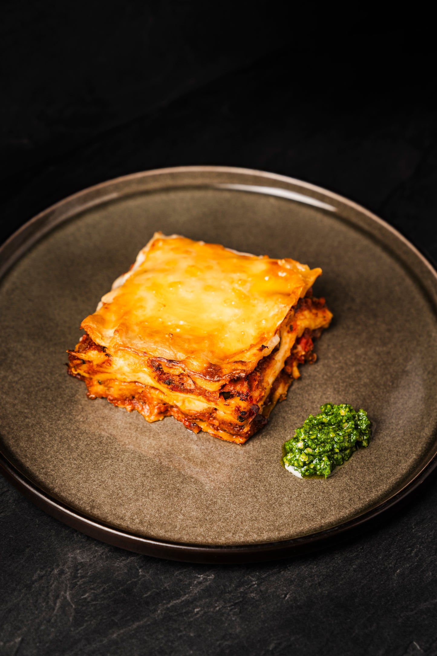 Lasagne mit gebackener Decke und grünem Kräuterpesto auf einem Teller